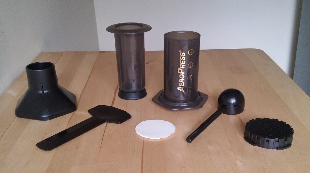 AeroPress contents (left to right: funnel, stirrer, top syringe cylinder, filter papers, bottom syringe cylinder, coffee scoop, filter cap)